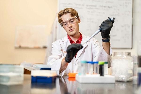 Student holding a pipette in a research lab.